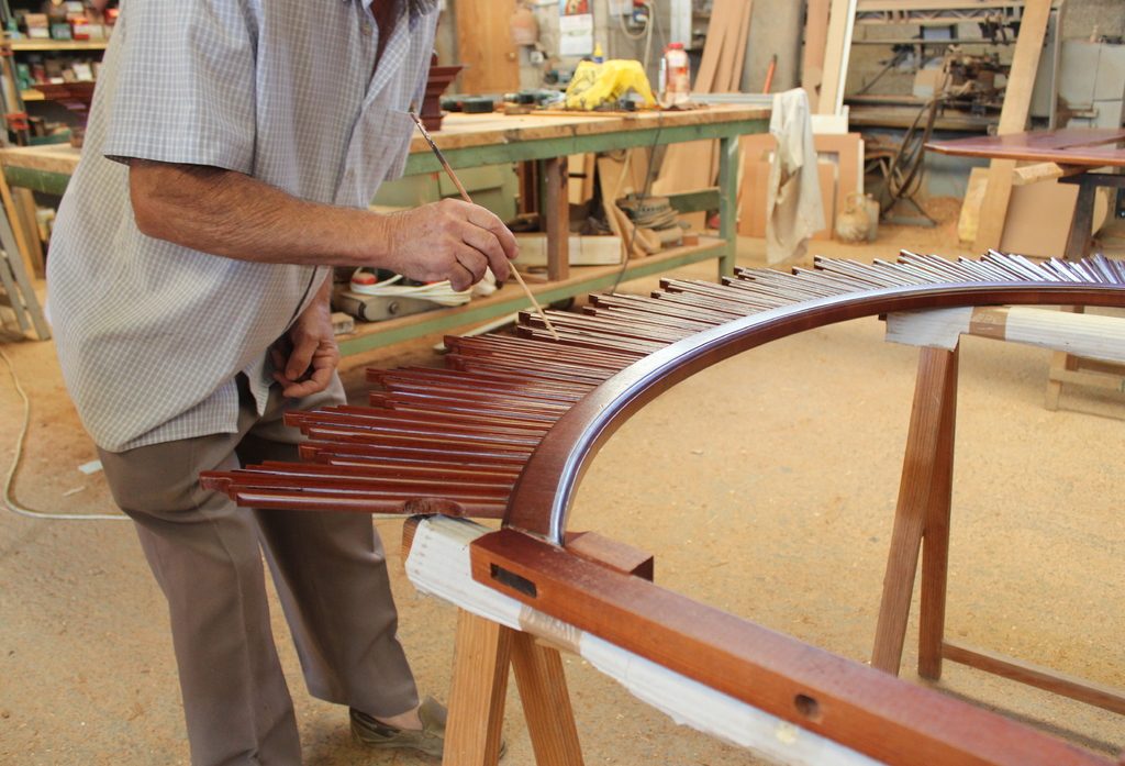 Craftsman shaping a curved wooden frame in a busy workshop