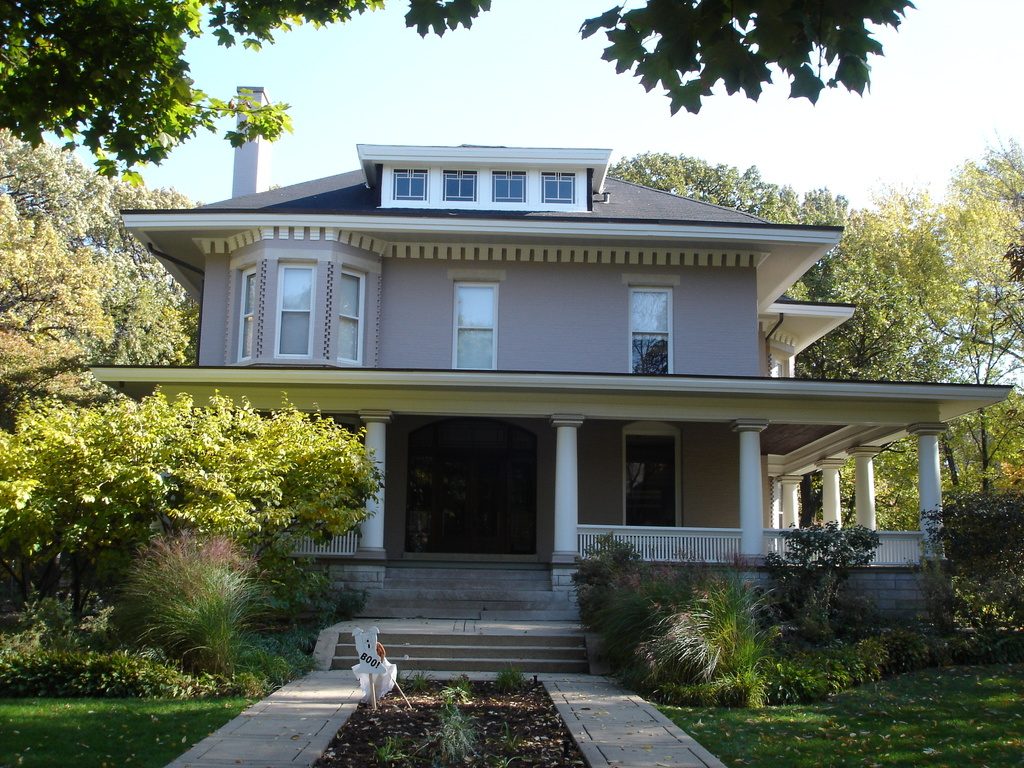 Two-storey prairie-style home with a wide front porch and lush landscaped garden