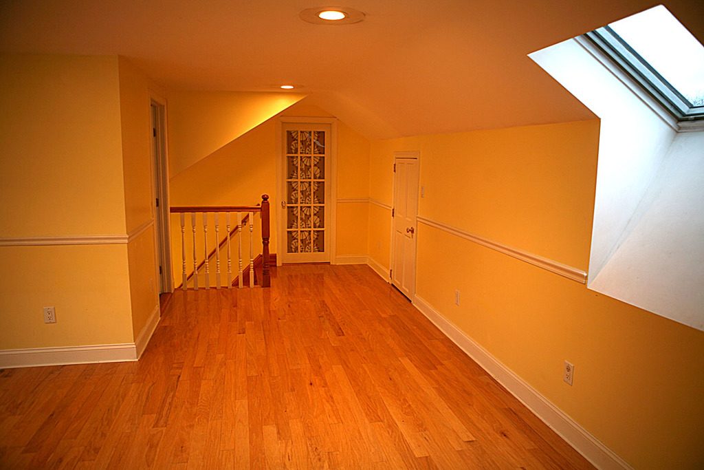 Sunlit upstairs hallway with honey-toned hardwood floors and a skylight
